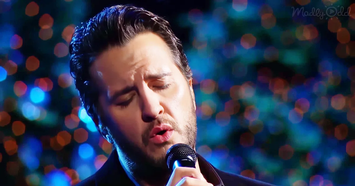 A man with dark hair and a beard sings into a microphone against a colorful, bokeh-lit background.