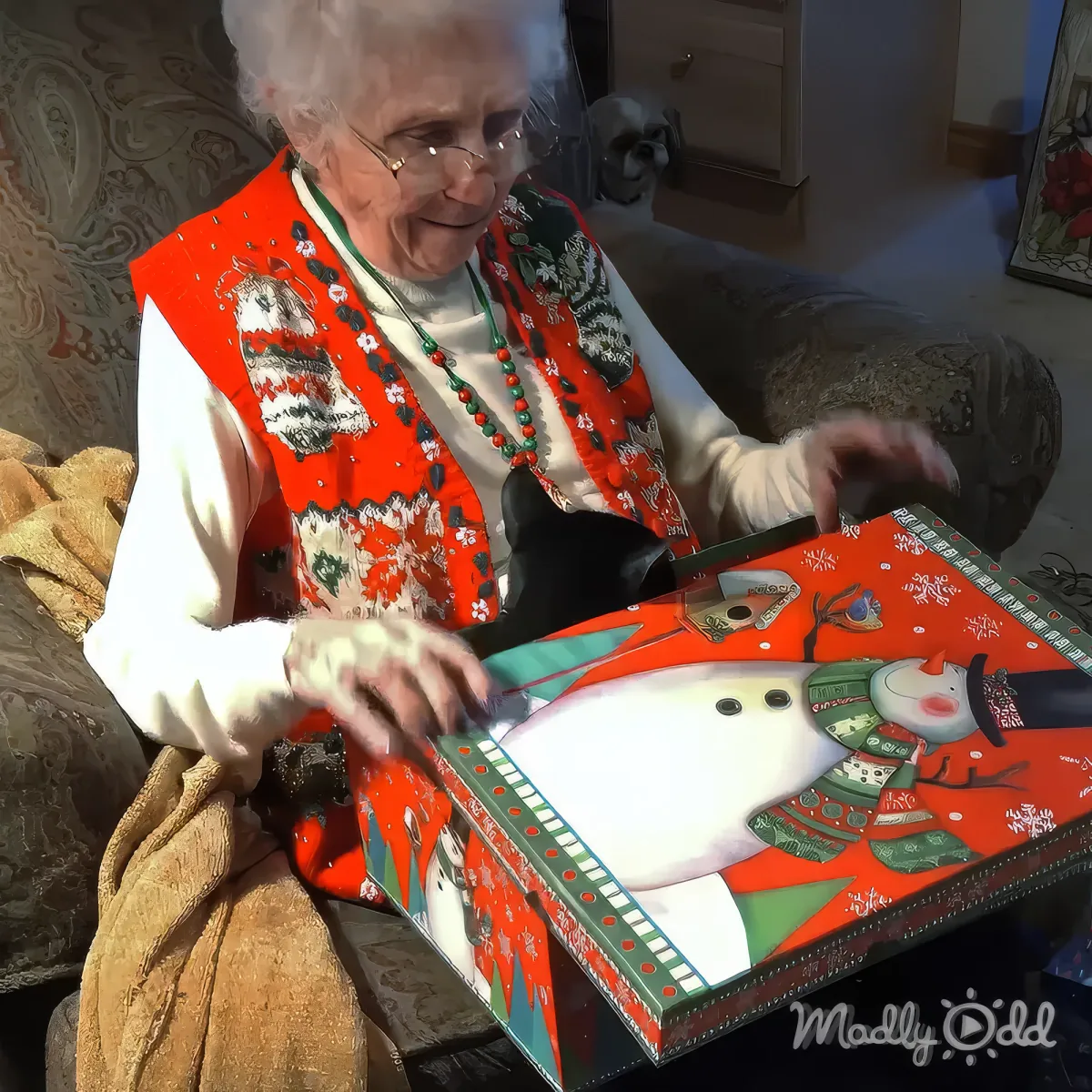 An elderly woman in a festive vest opens a Christmas-themed box with a snowman design.