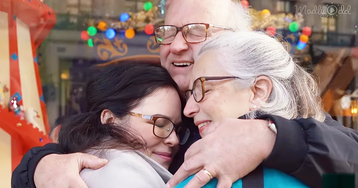 A woman hugs two older individuals in a festive setting with colorful lights.