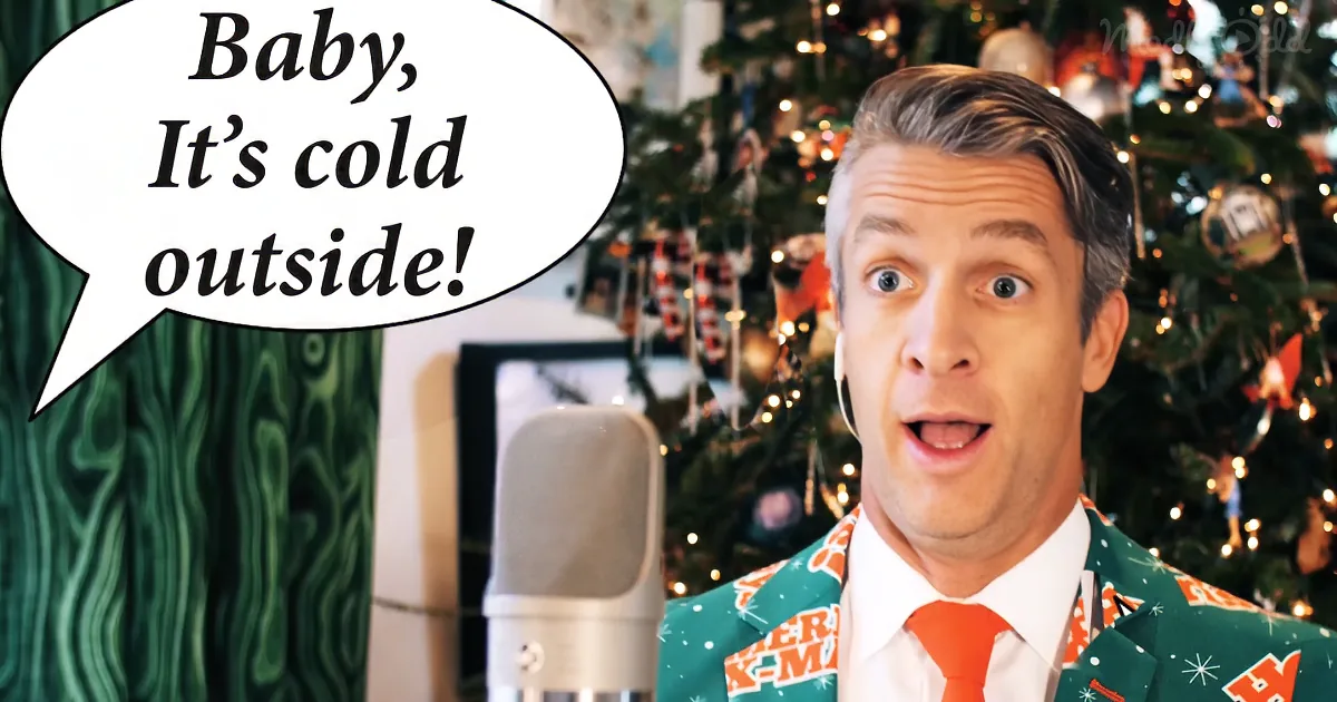 A man in a festive suit sings "Baby, It's cold outside" in front of a Christmas tree.