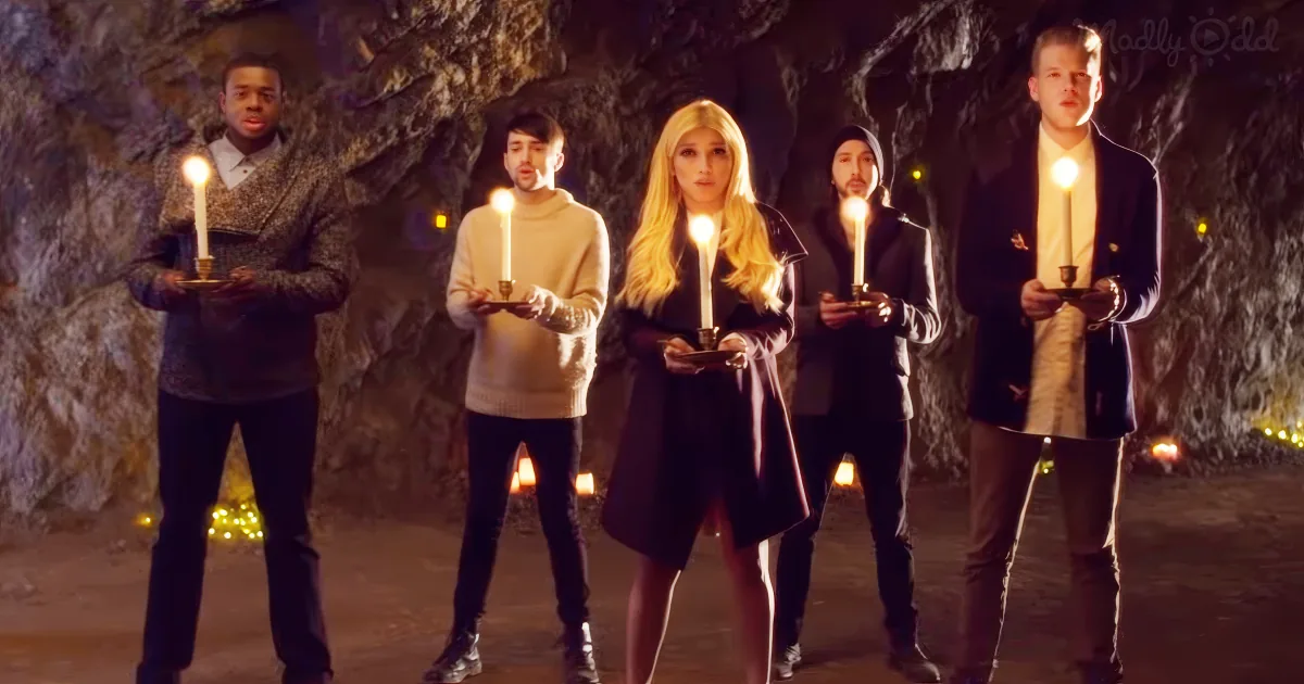 Five people stand in a cave holding lit candles, dressed in winter attire.