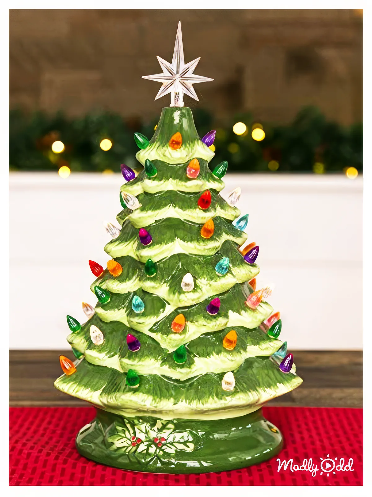 A ceramic Christmas tree adorned with colorful lights and a star on top, displayed on a red cloth.