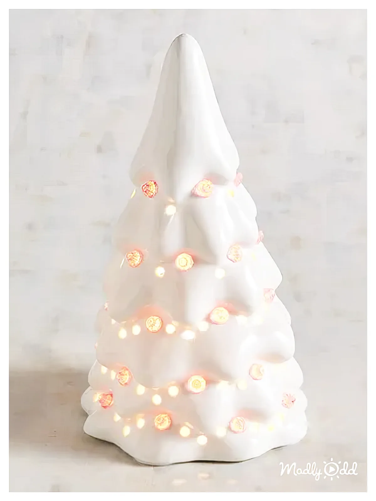 A white ceramic Christmas tree adorned with warm fairy lights sits on a marble surface.