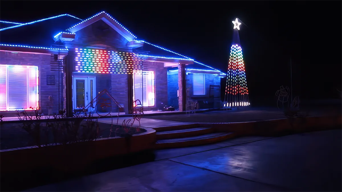 A house adorned with colorful lights and a tall Christmas tree with a star on top stands illuminated at night.