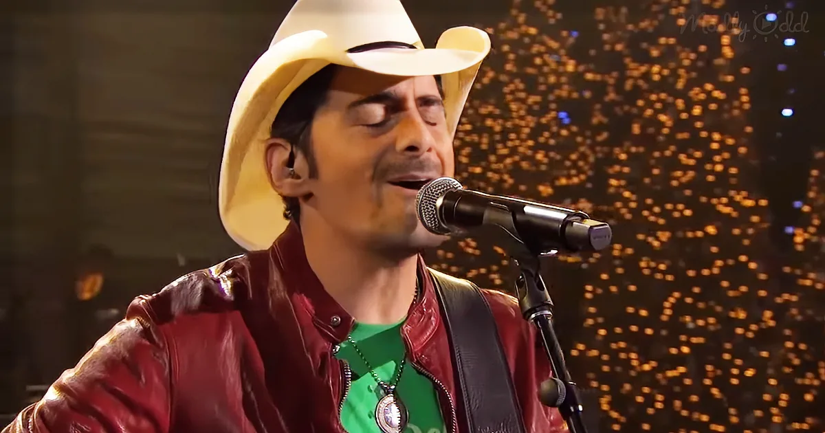 A man in a cowboy hat and red leather jacket sings into a microphone on stage.