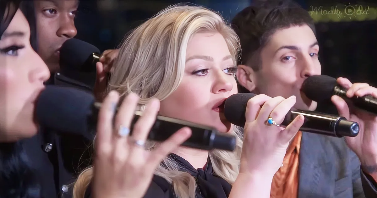 A woman sings passionately into a microphone, surrounded by other performers.