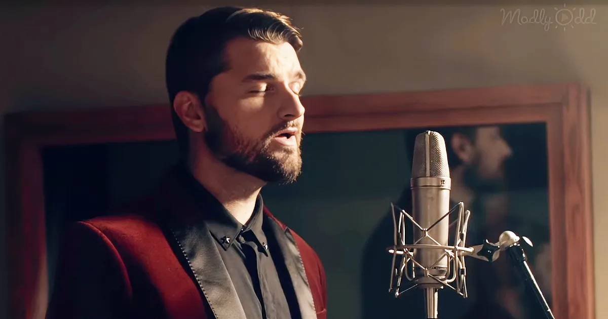 A man in a red suit sings into a microphone, his eyes closed, in a warmly lit room.