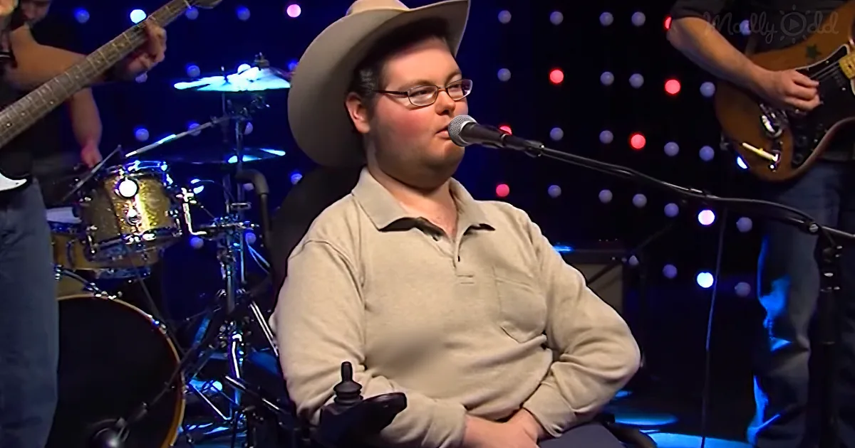 A man in a cowboy hat sings into a microphone on stage, surrounded by musicians and colorful lights.
