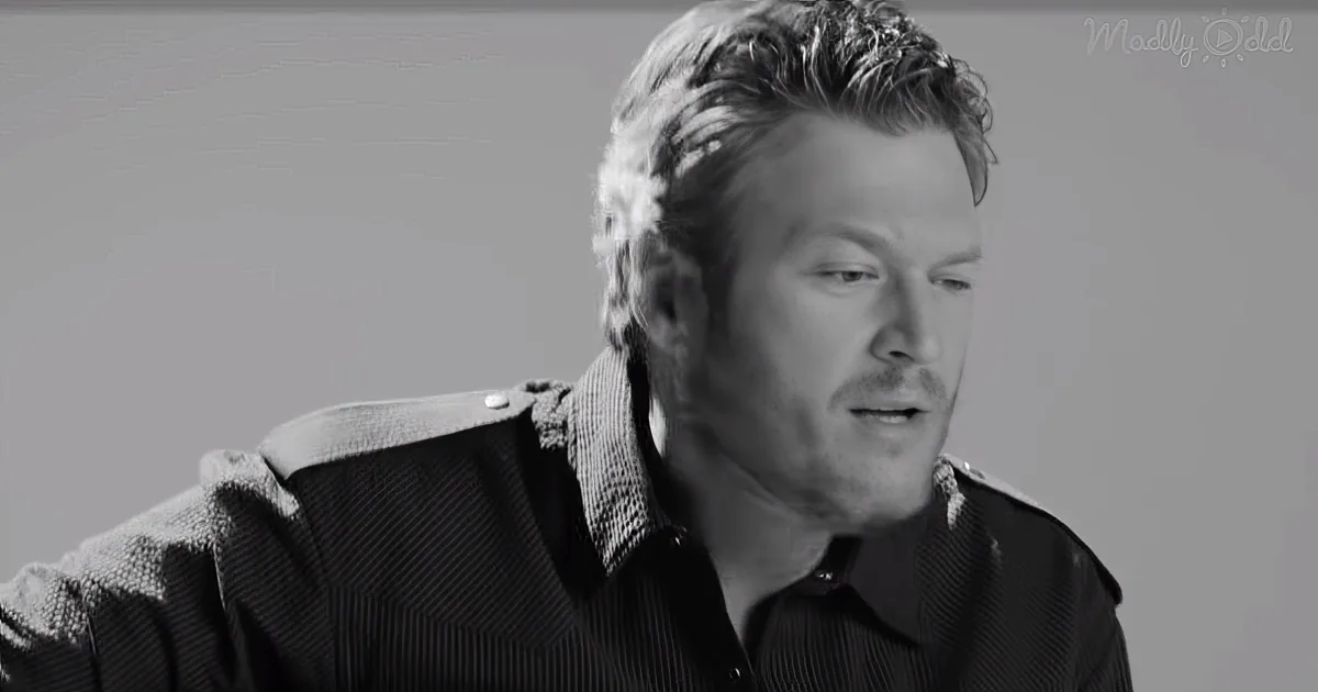 A man with short, styled hair wearing a dark shirt, looking downward in a grayscale image.