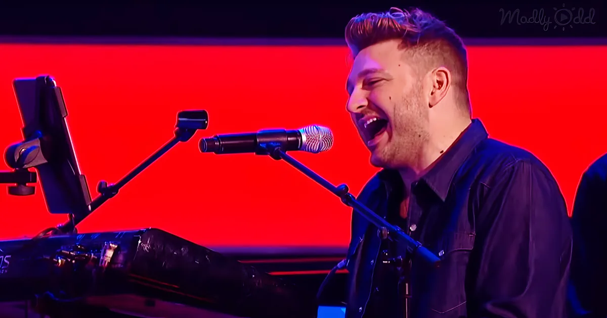 A man sings passionately into a microphone, illuminated by red and blue stage lighting.