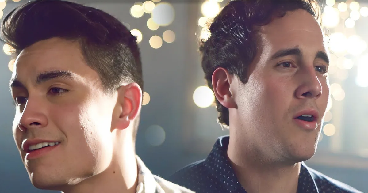 Two men, one smiling, the other speaking, against a blurred background of lights.