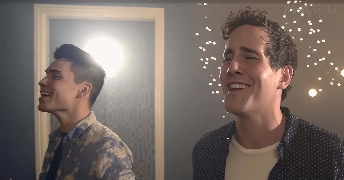 Two men smile, one in a patterned shirt, another in a polka dot shirt, with string lights in the background.