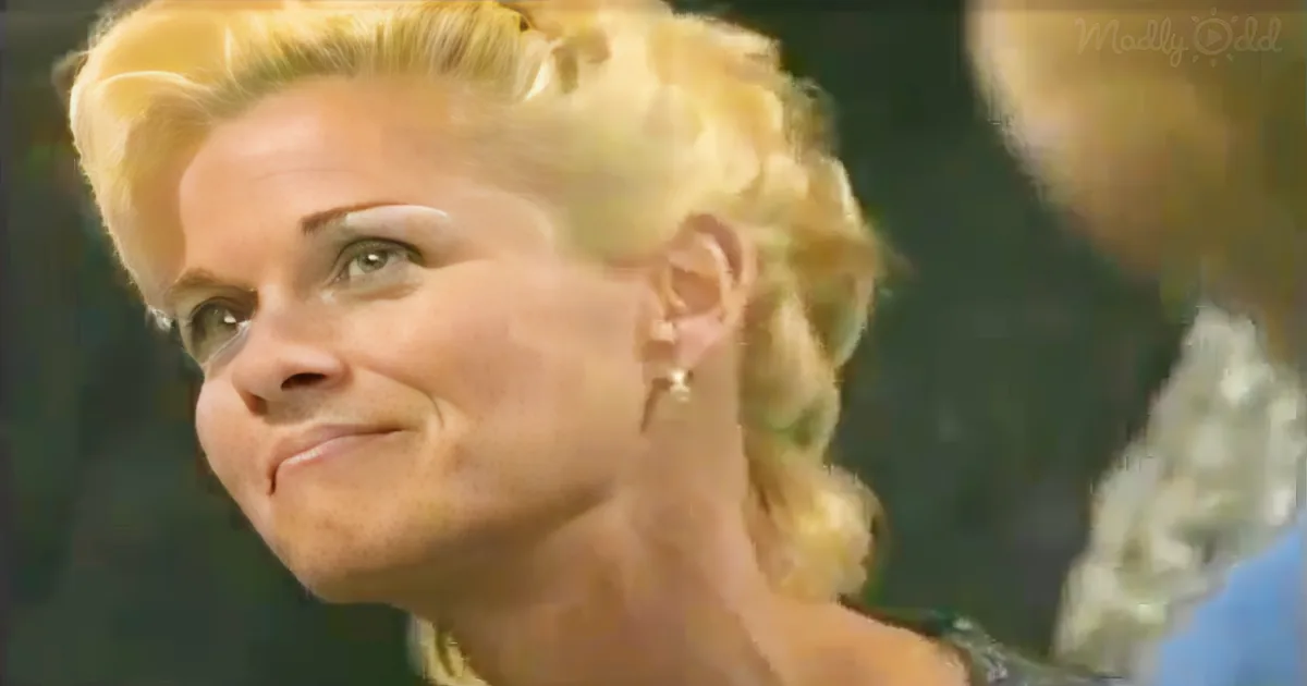 A woman with blonde hair styled in a braid, wearing earrings, and a green top is seen in a close-up shot.