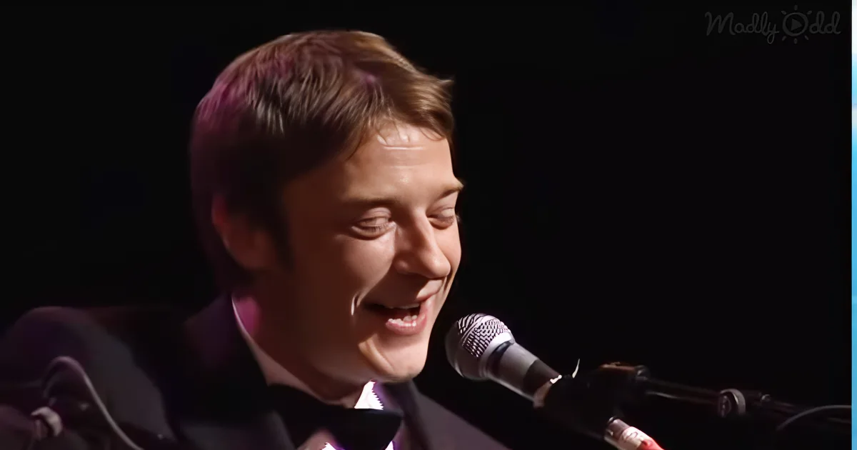 A man in a suit smiles while singing into a microphone on stage.