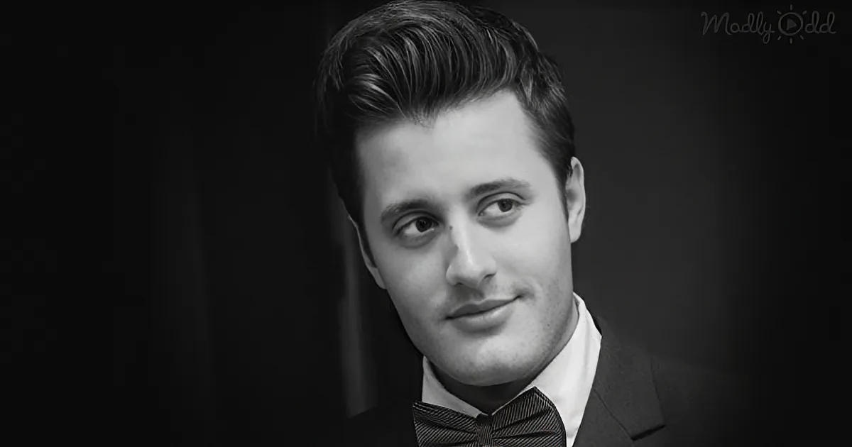 A man in a suit and bow tie, looking to the side, with a dark background.