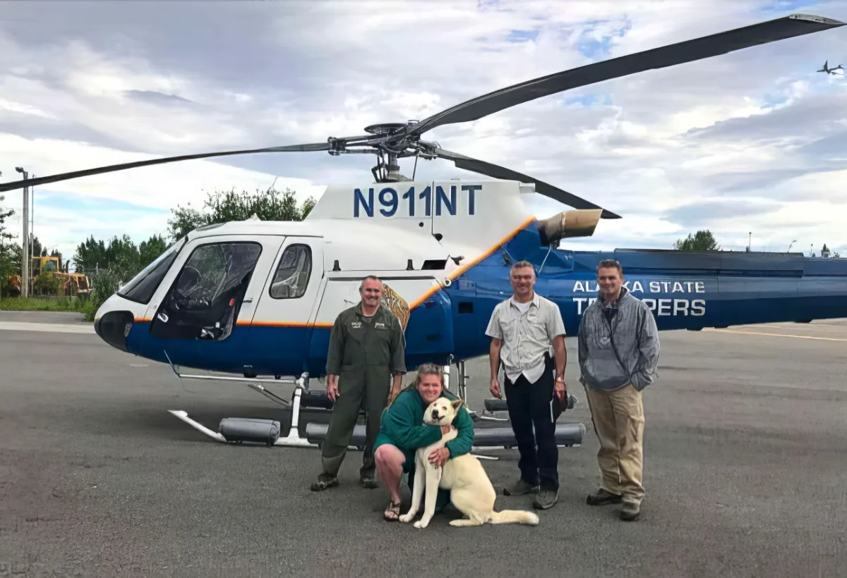 A group of people and a dog pose in front of a blue and white helicopter labeled "N911NT."