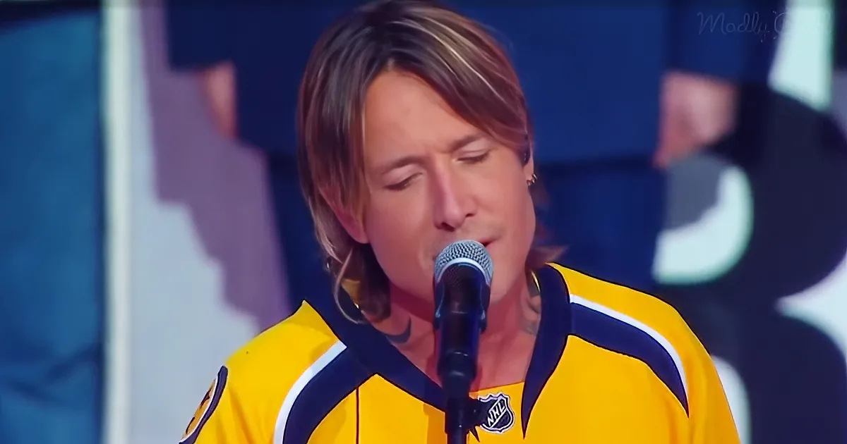 A person in a yellow jersey sings into a microphone, wearing a tattoo on their neck.