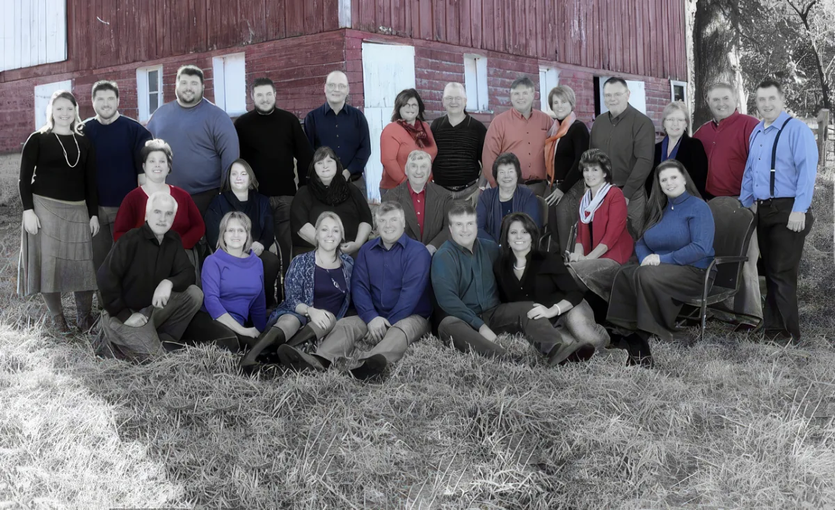 A group of people in colorful attire poses for a photo in front of a red barn.