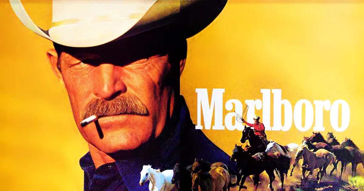 A cowboy with a cigarette in his mouth, wearing a white hat, with a herd of horses and the Marlboro logo in the background.