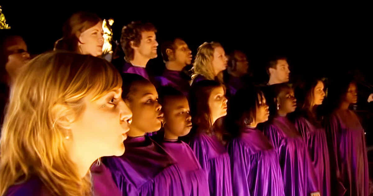 A choir in purple robes sings in unison, illuminated by a warm light.