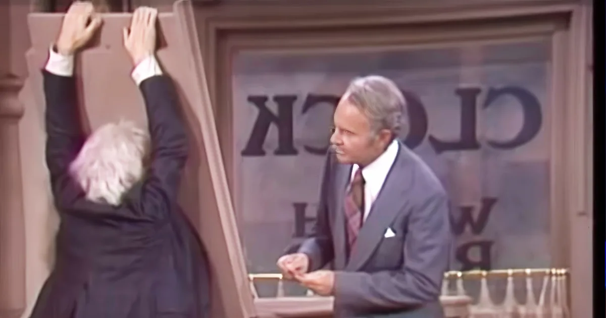 A man in a suit leans against a door frame, while another man in a suit stands nearby, looking at him.