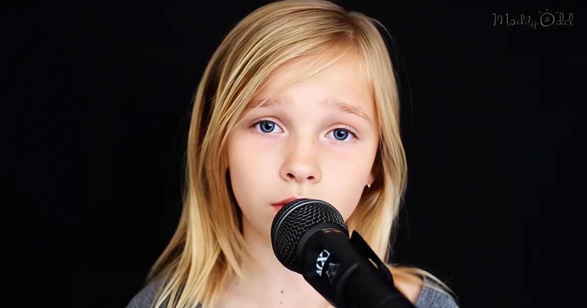 A young girl with long blonde hair sings into a microphone against a dark background.