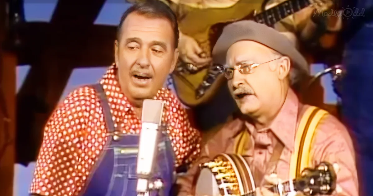 Two men in colorful attire sing into a microphone, one playing a guitar, in a lively performance setting.