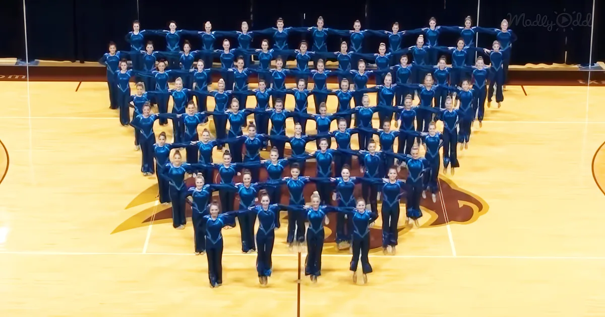 A synchronized dance team in blue uniforms performs a formation on a basketball court.