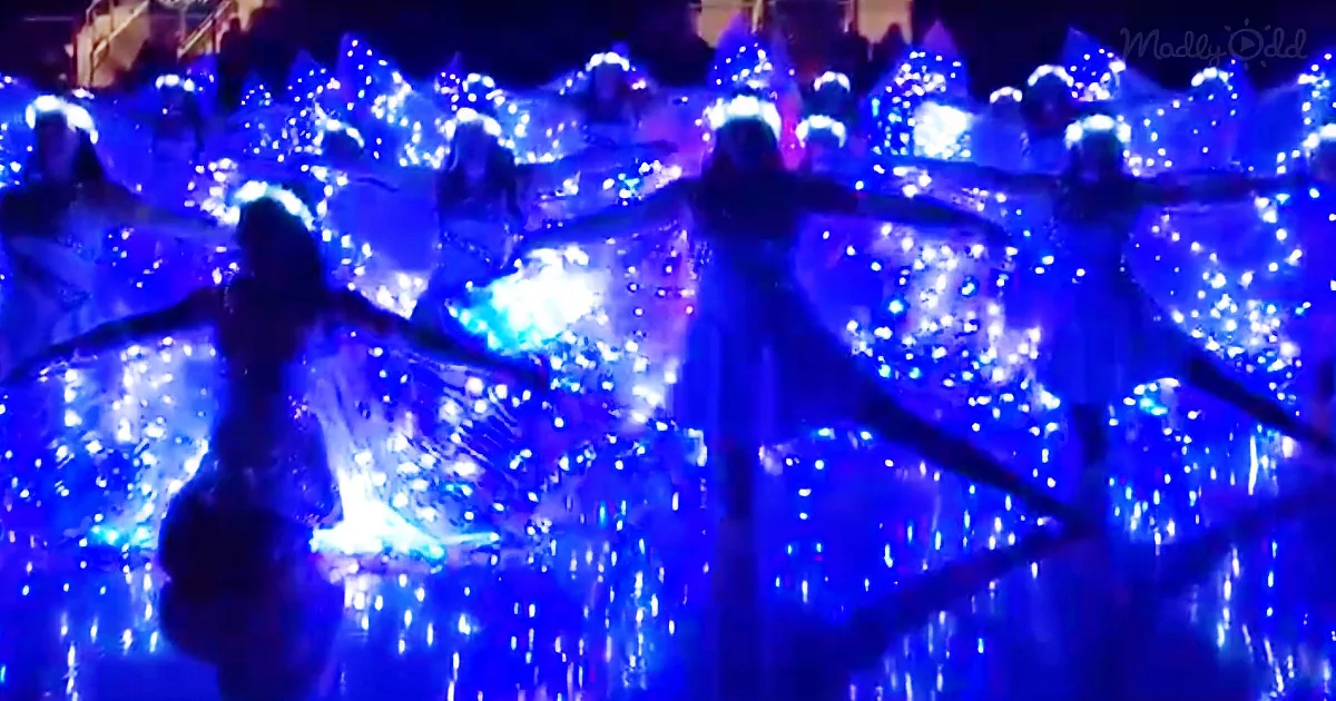 Dancers in glowing blue costumes perform with illuminated wings, creating a mesmerizing visual spectacle.