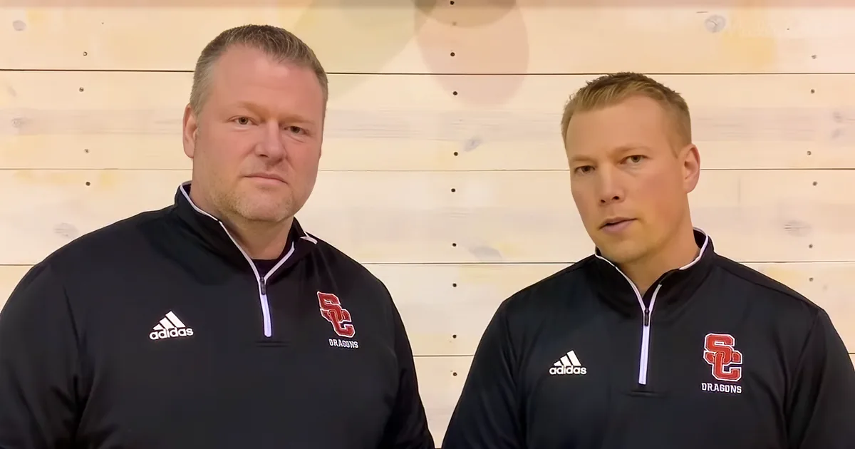 Two men in black Adidas jackets with "SC Dragons" logo stand side by side against a wooden wall.