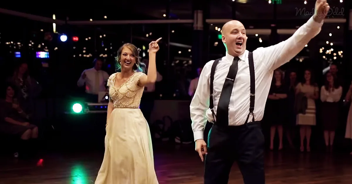A man and woman in formal attire dance joyfully on a dance floor, surrounded by guests and colorful lights.