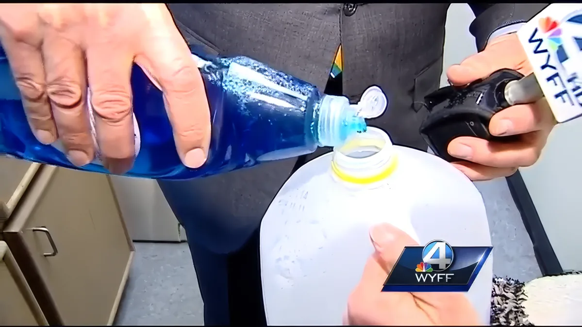 A person pours blue liquid from a bottle into a white container while holding a device.