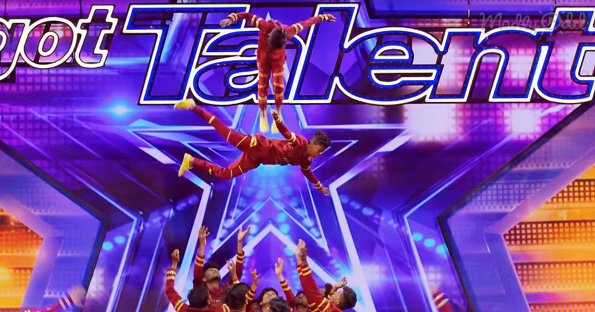 A performer is suspended mid-air above a group of acrobats in a "Got Talent" setting.