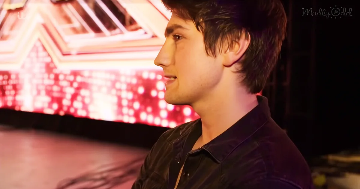 A man in a black shirt looks to the side, with a red-lit background and a logo in the corner.