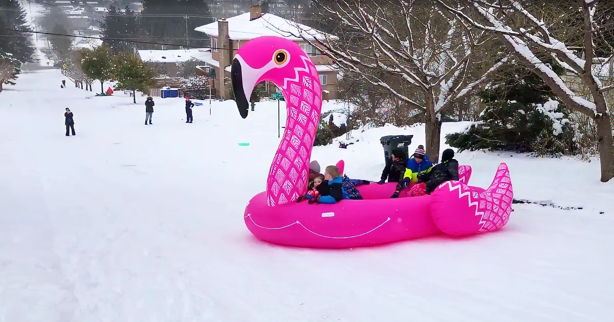 Children play on a pink inflatable flamingo in the snow.