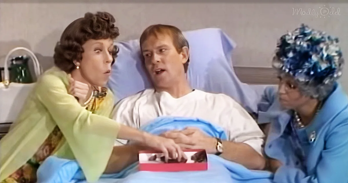 A woman in a green dress leans over a man in a hospital bed, holding his hand, while another woman in a blue outfit looks on.