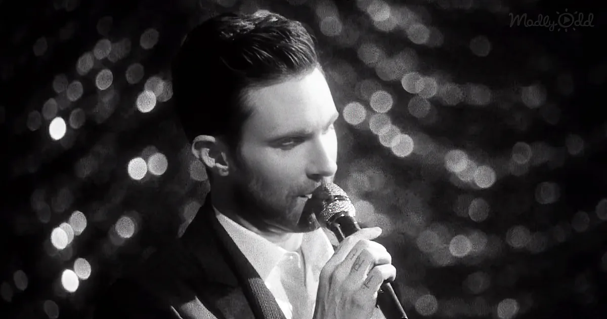 A man in a suit sings into a microphone, surrounded by blurred lights.