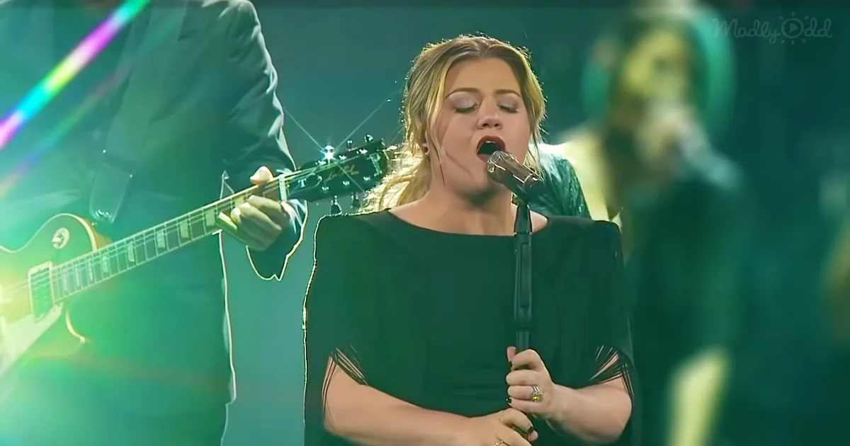 A woman in a black dress sings into a microphone on stage, surrounded by musicians.