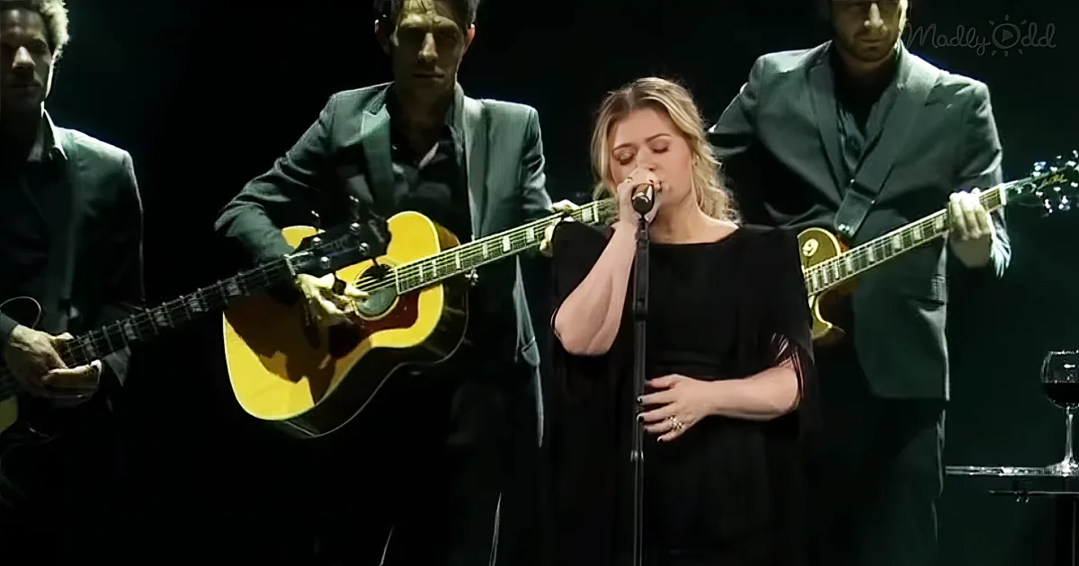 A woman sings into a microphone, flanked by musicians playing guitars and a bass.