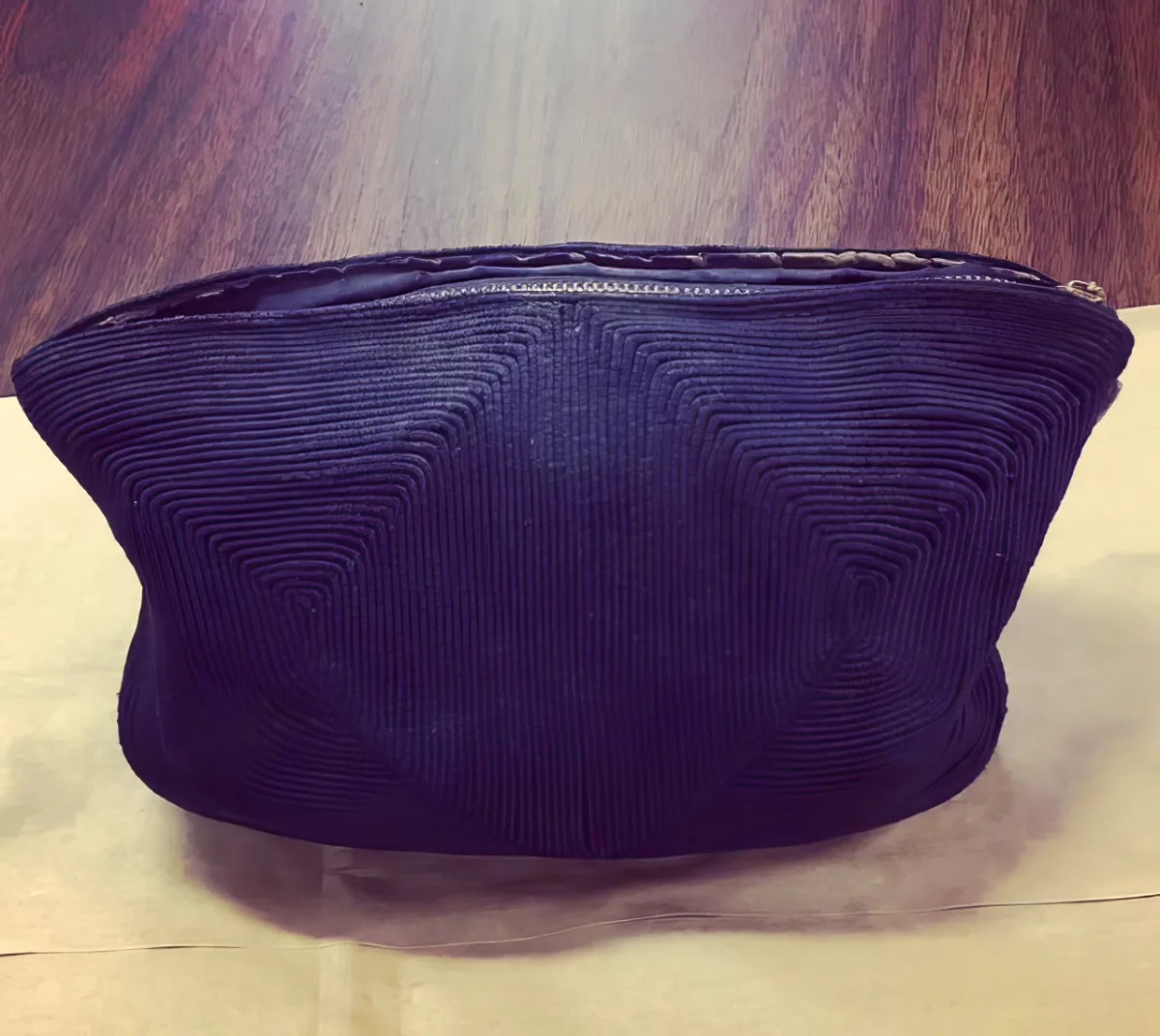 A dark purple, textured fabric pouch with a zipper lies on a wooden surface.