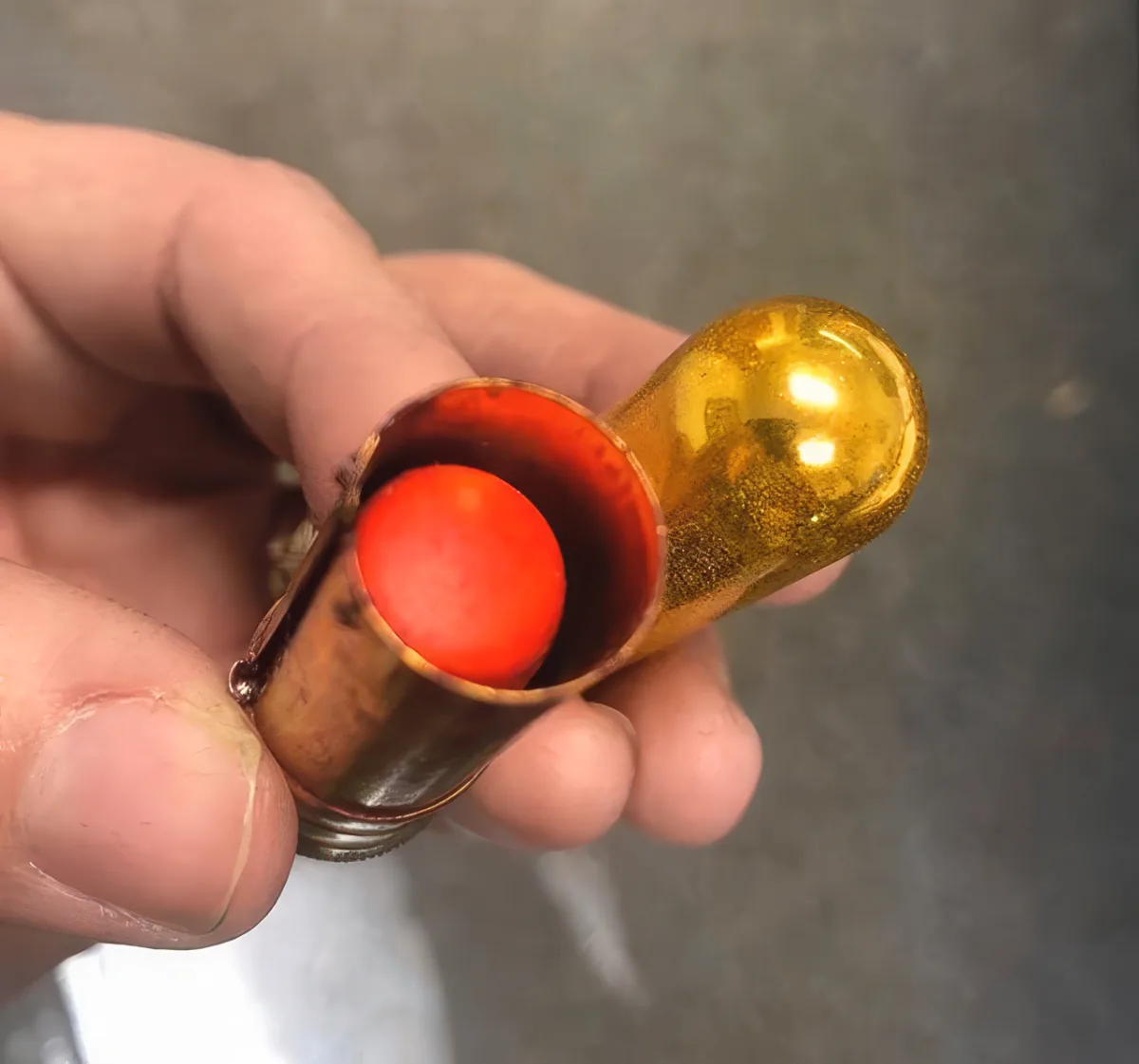 A hand holds a brass object with a red interior, resembling a small mechanical or decorative piece.