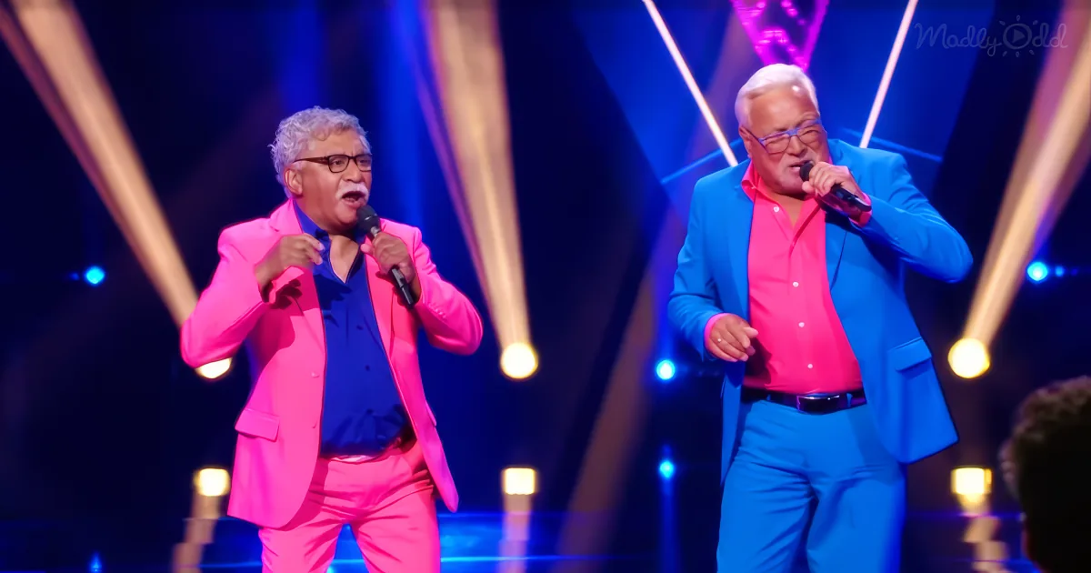 Two men in bright suits sing on stage with colorful lights behind them.