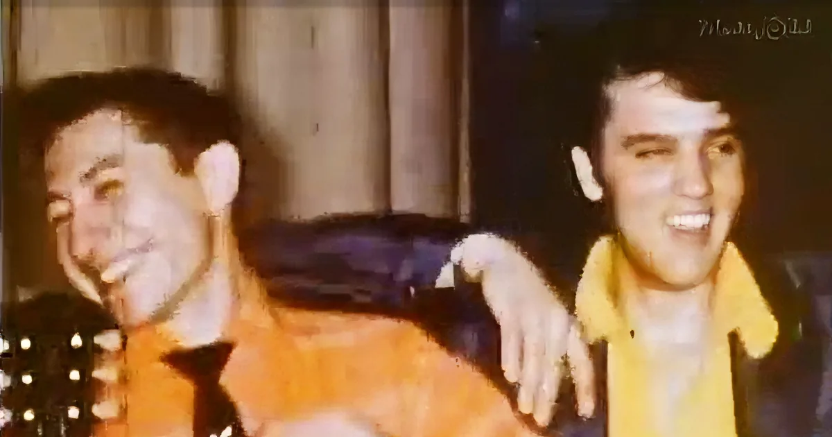 Two men in orange shirts smile and pose together, one has his arm around the other.