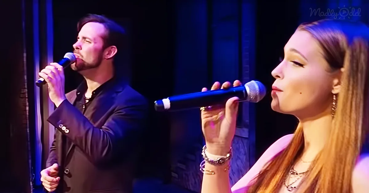 A man and a woman are singing into microphones on stage under blue lighting.