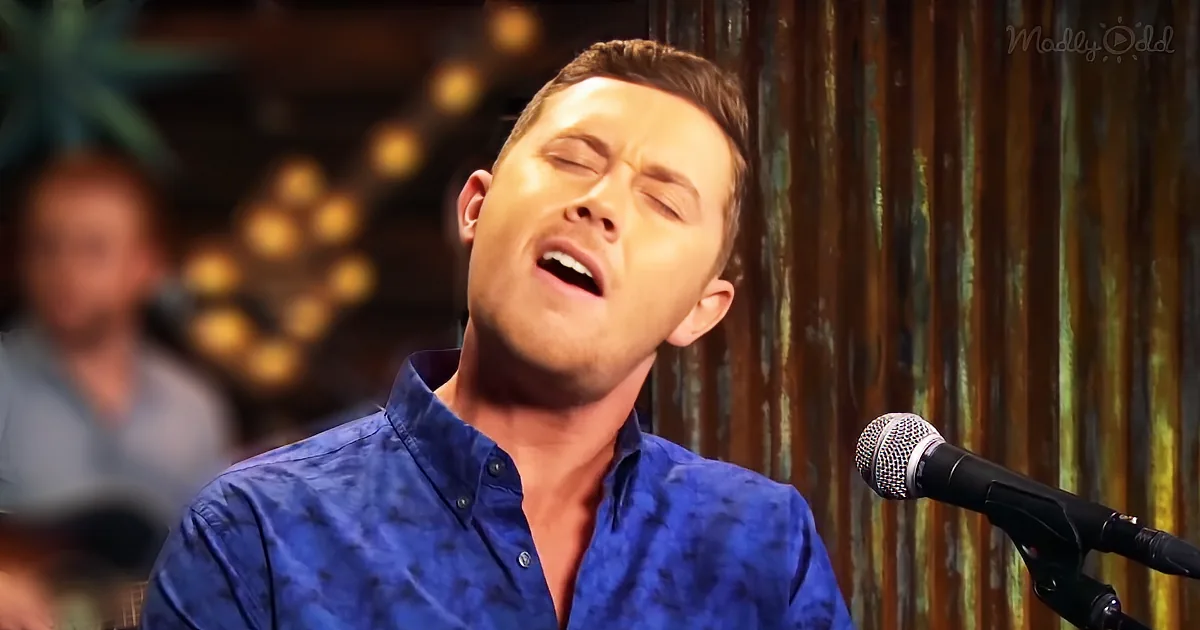 A man in a blue shirt sings passionately into a microphone, eyes closed, with a band in the background.