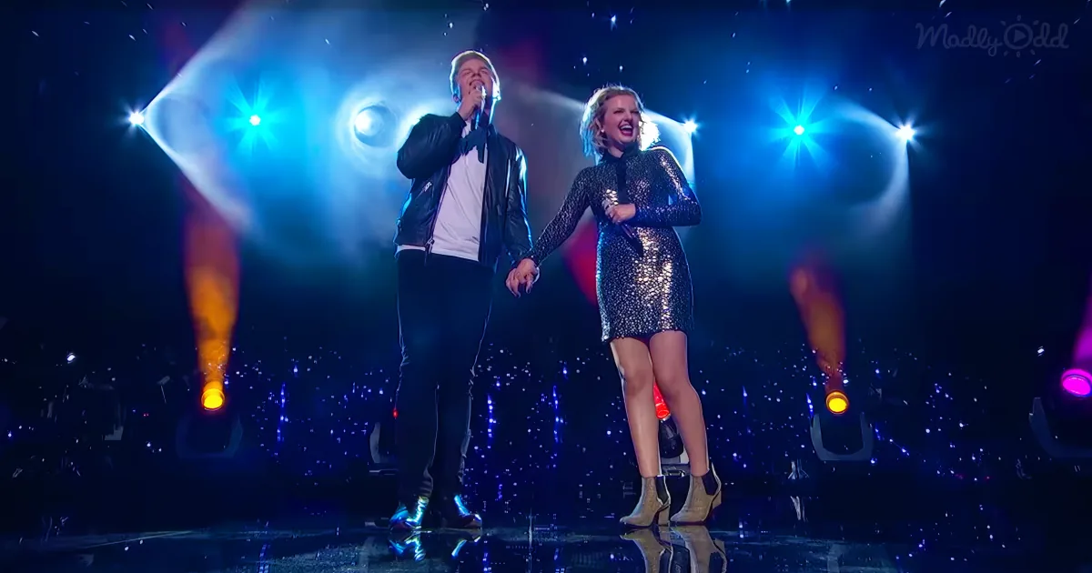A man and woman sing on stage under bright lights, holding hands, in a vibrant performance.