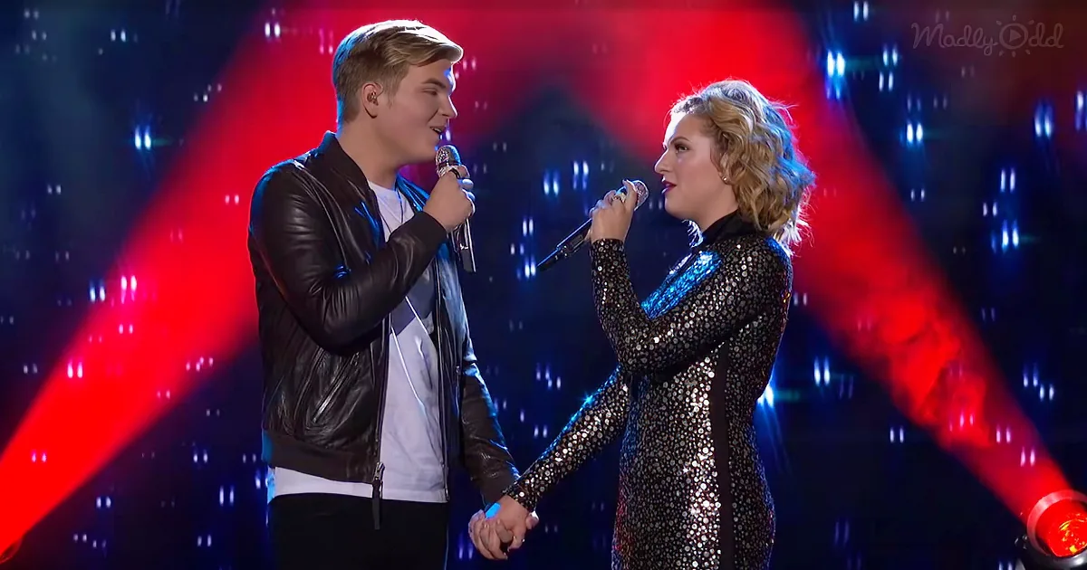 A man and woman sing on stage, holding hands, with red and blue lights behind them.
