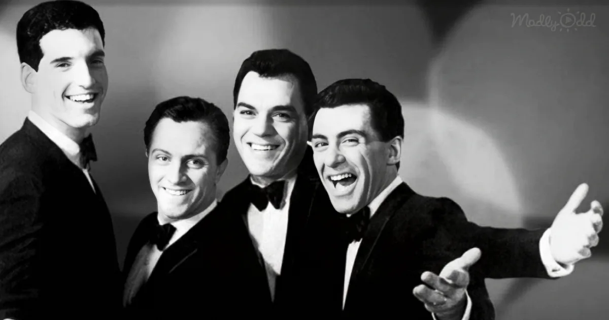 Four men in tuxedos smile and pose together, one pointing dramatically.