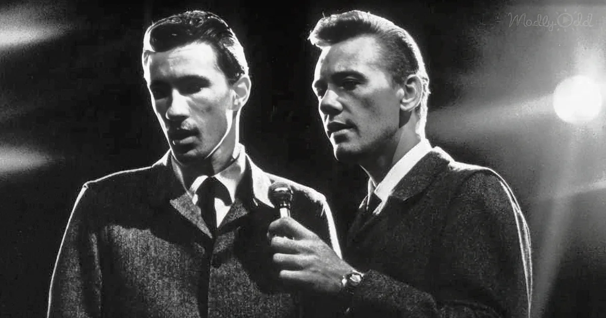 Two men in suits, one holding a microphone, standing close, possibly on stage or in a studio.