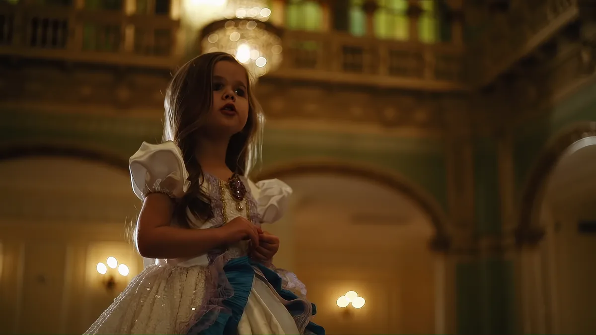 A young girl in a white dress stands in a grand, ornate room with arched ceilings and chandeliers.